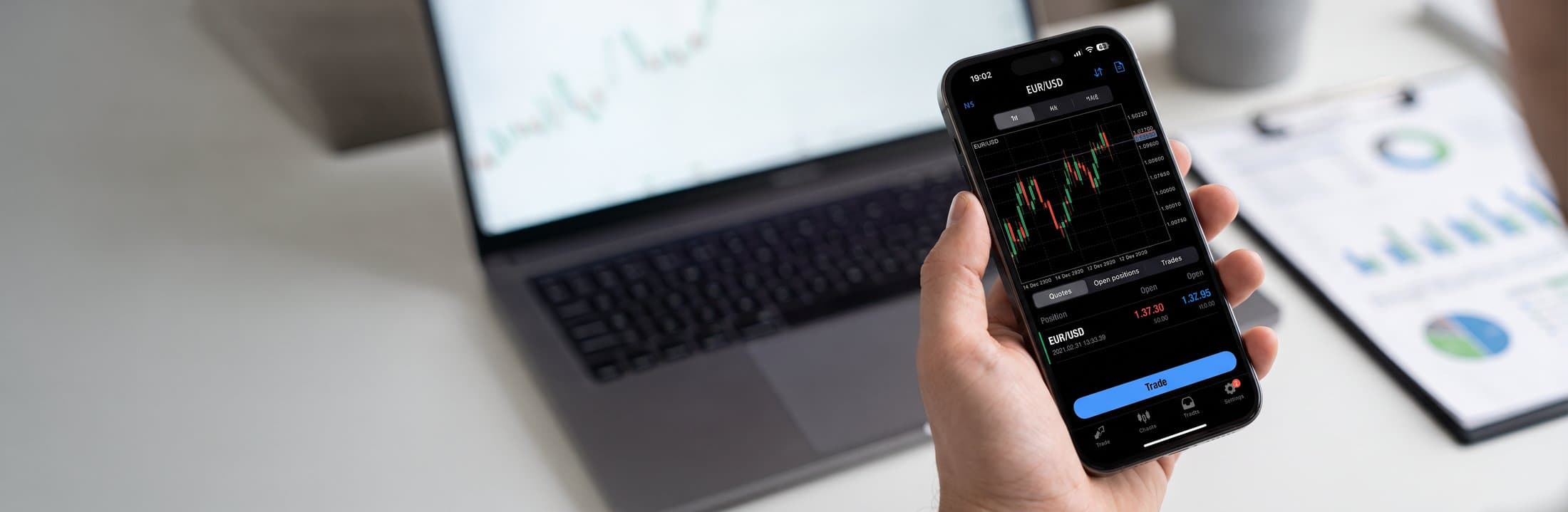 Trader checking EUR/USD prices on a phone beside a laptop