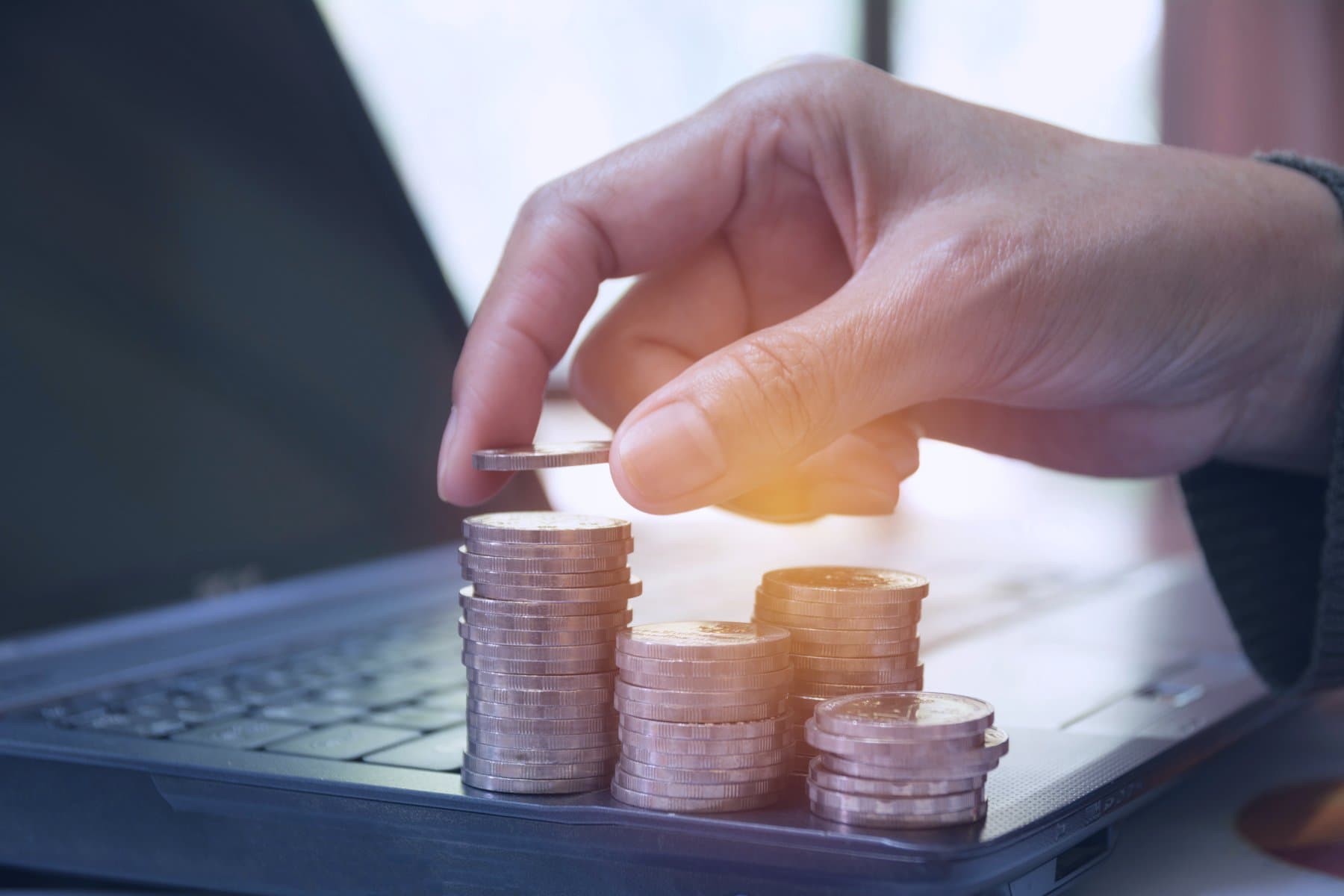 Hand stacking coins beside a laptop, illustrating growing financing costs